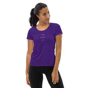 May include: A purple athletic t-shirt with a scoop neck and short sleeves. The shirt has the text "In my perfect era" printed in a darker purple color. The model is wearing black leggings.