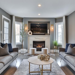 Puede incluir: Una sala de estar con dos sofás grises, una chimenea de mármol blanco con fuego encendido, una mesa de café con base dorada y un gran espejo en la pared.