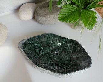 May include: A green marble soap dish with a hole in the center. The dish is oval shaped and has a rough, natural texture.