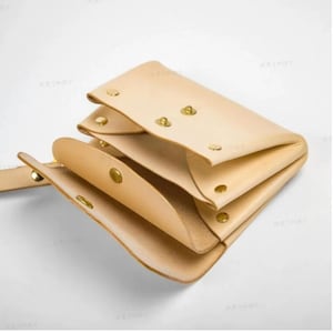 Può includere: Un portafoglio in pelle marrone chiaro con più scomparti e bottoni a pressione in ottone. Il portafoglio è aperto e l'interno è visibile.