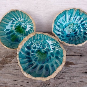Könnte beinhalten: Drei tealblaue Keramikschalen mit einem strukturierten, erhabenen Design. Die Schalen haben einen hellbraunen Rand und sind in einem dreieckigen Muster angeordnet.