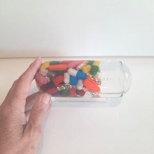 May include: A clear glass bottle filled with a variety of colourful capsules and pills. The bottle is partially filled with liquid.