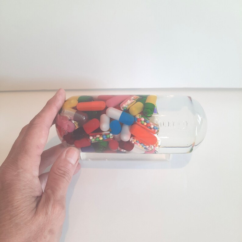 May include: A clear glass bottle filled with a variety of colourful capsules and pills. The bottle is partially filled with liquid.