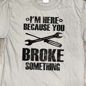 May include: A gray t-shirt with a black graphic that says "I'm here because you broke something" with a pair of crossed wrenches.