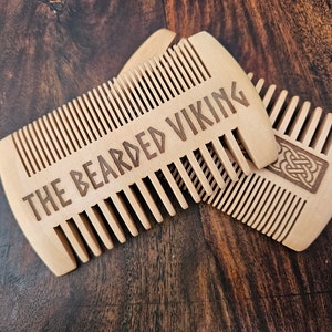 May include: Two wooden combs, one with the text "The Bearded Viking" and the other with a Celtic knot design.