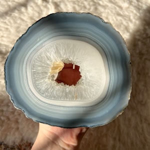 May include: A large, white agate geode slice with a natural hole in the center. The geode has a gray outer edge and white and gray banding.