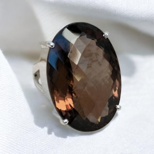 May include: A silver ring with a large, oval-shaped, faceted, brown gemstone.