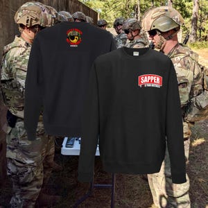 May include: Black long-sleeve sweatshirt with a red and white "SAPPER" graphic on the front. The graphic includes the text "K YOUR OBSTACLE".