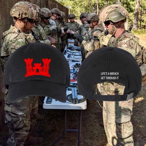 May include: Two black baseball caps. One cap features a red embroidered castle logo. The other cap has the text "Life's a breach get through it" embroidered in white.