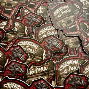 May include: A stack of stickers featuring a black and green camouflage helmet with a red outline. The helmet has a red and white scope attached to it. The text "CONVENTIONAL AS Fark" is written in white on a black background. The stickers are all identical and are arranged in a random pattern.