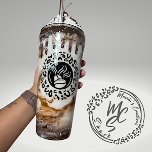 K&ouml;nnte beinhalten: Ein hoher Becher im Design eines Schokoladen-Milchshakes mit wei&szlig;em Glitzer-Untergrund, braunen Wirbeln, dunklem Schokoladenguss-Effekt, bunten Streuseln und einer k&uuml;nstlichen Schlagsahne-Haube mit Kirsche. Vorne ist ein schwarzes, kreisf&ouml;rmiges Logo mit Leopardenmuster und Kaffeebohnen-Grafik abgebildet.