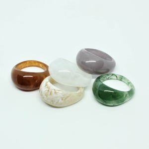 May include: Five chunky rings in various colours are displayed against a white background. The rings include shades of brown, white, grey, green, and a marbled beige. The rings have a smooth, rounded design, suitable for everyday wear.
