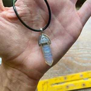 May include: A white opal crystal pendant on a black leather cord. The crystal is wrapped in silver wire and has a silver cap on the top.