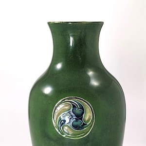 May include: A green ceramic vase with a circular design featuring stylised leaves and flowers in shades of blue, green, and white.