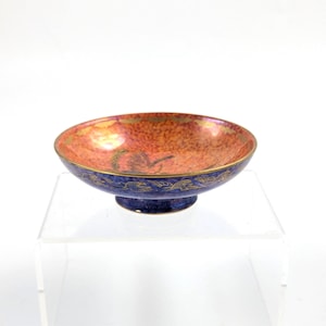 May include: A small, blue and orange ceramic bowl with gold accents. The bowl has a footed base and a scalloped rim.