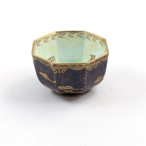 May include: A small, octagonal, dark purple bowl with gold accents and a light blue interior. The bowl has a decorative design around the rim and a floral pattern on the exterior.