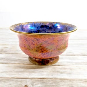 May include: A small, iridescent ceramic bowl with a footed base. The bowl has a blue and purple glaze with a speckled effect. The bowl is decorated with gold butterfly designs.
