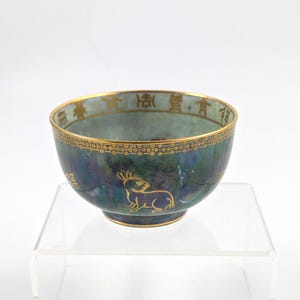 May include: A small, blue and green ceramic bowl with gold trim and a rabbit design. The bowl has Chinese characters around the rim.