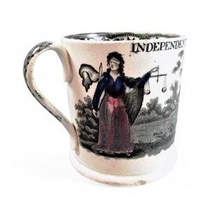 Könnte beinhalten: Eine weiße Keramiktasse mit schwarzem Henkel. Die Tasse zeigt ein Schwarzweißbild einer Frau, die eine Waage und ein Schwert hält. Der Text "INDEPENDENT" ist auf die Tasse gedruckt.