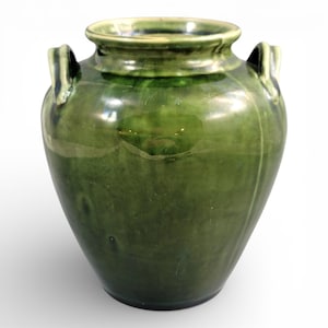 Pode incluir: Um vaso de cerâmica verde com duas pequenas alças. O vaso tem um acabamento brilhante e uma forma arredondada, com uma borda ligeiramente alargada. A cor é um verde profundo e rico, com variações de tom na superfície.