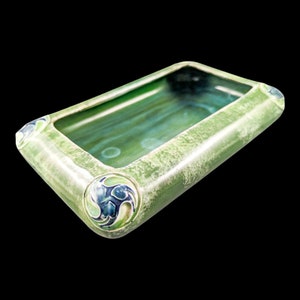 May include: A rectangular ceramic dish with a green glaze and blue and white floral designs. The dish has a slightly raised rim and a shallow interior.