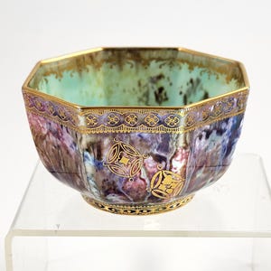 May include: An octagonal ceramic bowl with a gold rim and decorative gold accents. The bowl features a watercolor-like design in shades of purple, blue, and green. The interior has a green and brown marbled effect.