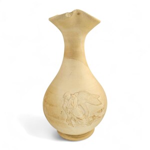 May include: A beige-colored vase with a wide, flared top and a rounded body. The vase features an embossed design of a winged figure. The vase is made of a light-colored material, possibly ceramic or stone, and has a smooth finish.