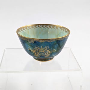 May include: A small, teal blue ceramic bowl with gold trim and a gold design on the bottom. The design features a crown and the words "SIGILLVM REGIS".