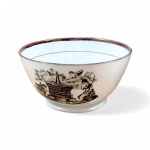 May include: A white porcelain bowl with a brown and black design of a scene with a building, figures, and clouds. The bowl has a gold rim.