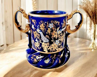 Könnte beinhalten: Eine kobaltblaue Keramikvase mit goldenen Akzenten und einem Pfauenmuster. Die Vase hat zwei Henkel und einen wirbelnden Sockel.