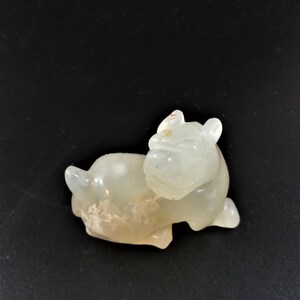 May include: A white jade carving of a reclining dog. The carving is detailed and realistic, with a smooth, polished finish.