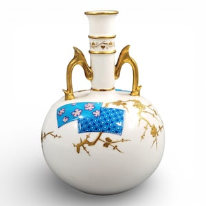 May include: A white ceramic vase with a round body and a tall, cylindrical neck. It features gold-coloured handles and floral accents. The vase has blue and pink floral designs and gold branches. The vase is approximately 25 cm tall.