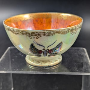 May include: A small, iridescent white bowl with a gold rim and a painted butterfly design. The bowl has a footed base and is decorated with gold accents.