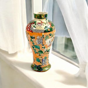 Puede incluir: Un jarrón de cerámica decorativo de color naranja y verde con un patrón floral. El jarrón tiene un cuello estrecho y una base ancha.