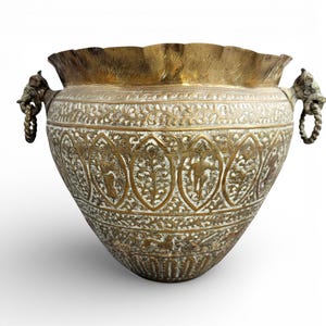 May include: An antique brass planter with intricate etched designs and a ruffled rim. The planter features detailed patterns and figures, with elephant head handles on each side. A decorative piece for home decor.