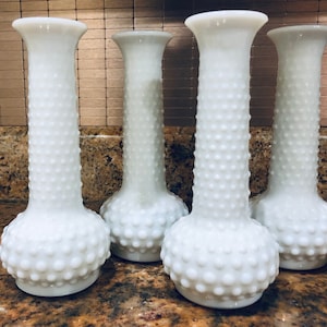 Könnte beinhalten: Set aus vier weißen Milchglas-Blumenvasen mit einem strukturierten, perligen Design. Die Vasen sind hoch und schlank mit einem abgerundeten Boden.