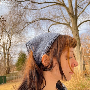 May include: A person with long brown hair wearing a light blue knitted bandana tied around their head. The bandana has a lace pattern around the edges. The person is wearing a black and white striped shirt.