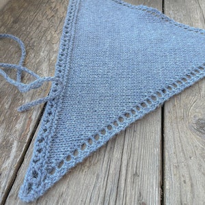 May include: A blue knitted triangle shawl with a crocheted border. The shawl is lying on a wooden surface.