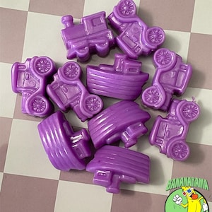Può includere: Una collezione di veicoli giocattolo in plastica viola, tra cui auto, treni e barche, sono sparsi su una superficie a scacchi. L'immagine include un logo con una banana dei cartoni animati con occhiali 3D.