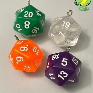 May include: Four polyhedral dice pendants in green, clear, orange, and purple. Each die has white numbering and a silver-coloured loop for hanging. The dice are for tabletop gaming.