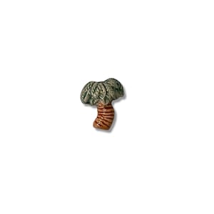 May include: A miniature ceramic palm tree figurine. The tree features a textured, green frond top and a brown, striped trunk. The figurine is a decorative item, likely for display or collection.