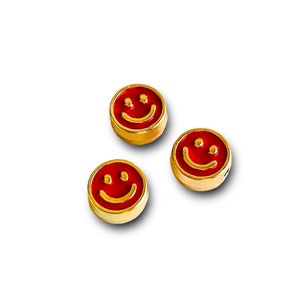 May include: Three gold-colored smiley face charms with red enamel faces. Each charm has a smiling mouth and two small dots for eyes. The charms are round and have a gold-colored border.