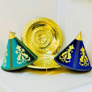 May include: Two decorative cone-shaped covers with gold embroidery on a blue and green background. The covers are sitting on top of two gold metal serving trays.