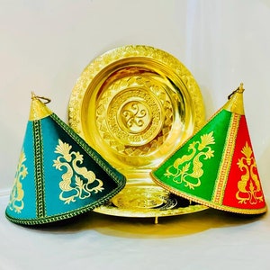 May include: Three decorative gold serving dishes with green and red fabric covers. The covers have gold embroidery and are shaped like cones.