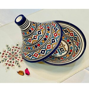 May include: A traditional Moroccan tagine with a blue and white base and a colourful geometric pattern. The lid is also decorated with a similar pattern.