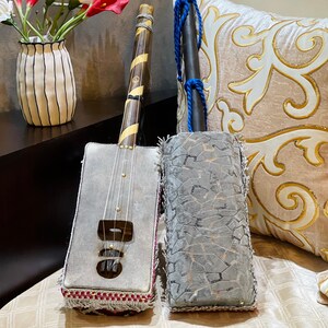 May include: Two musical instruments, one with a gray fabric body and a wooden neck, the other with a gray fabric body and a wooden handle. Both instruments are decorated with intricate patterns and have a tassel.
