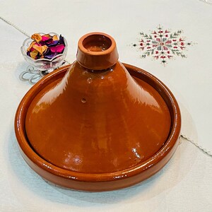 Könnte beinhalten: Eine Terrakotta-Tajine mit einem runden Boden und einem konischen Deckel. Die Tajine ist glasiert und hat eine glänzende Oberfläche.