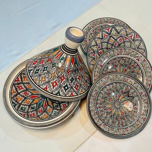 Può includere: Un set di sei piatti in ceramica e una zuppiera con coperchio decorata con intricati motivi geometrici in tonalità di verde, rosso, giallo e bianco su sfondo grigio.