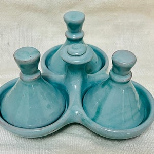 May include: A set of three teal ceramic condiment dishes with lids. The dishes are arranged in a triangular shape on a base.