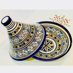 May include: A traditional Moroccan tagine with a blue and white base and a colourful geometric pattern. The lid is also decorated with a geometric pattern and has a pointed top.